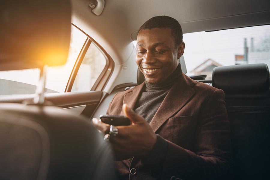 Client Center - Stylish Man Being Chauffeured While Using His Phone and Smiling
